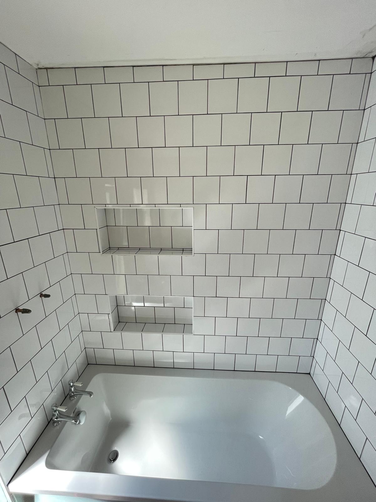 Wall tile installation above bath with in built wall shelving 