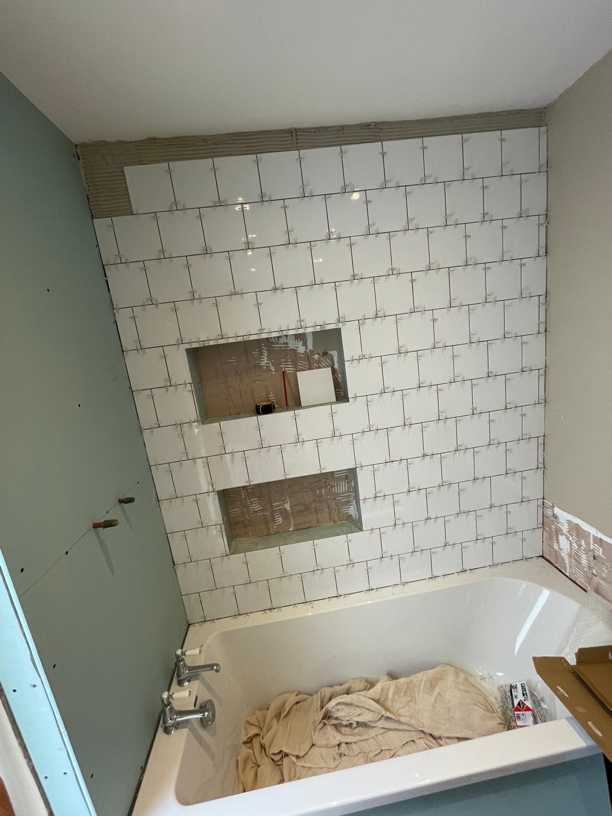 White square wall tile installation wall above bath nearly complete 